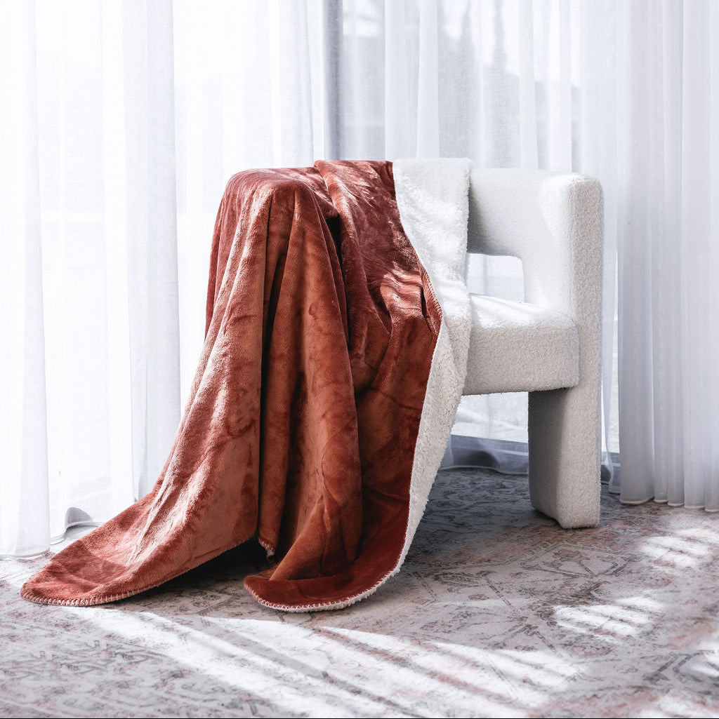 A plush waterproof throw blanket draped over a modern white armchair in a bright room with sheer white curtains and sunlight streaming through.