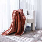 A plush waterproof throw blanket draped over a modern white armchair in a bright room with sheer white curtains and sunlight streaming through.